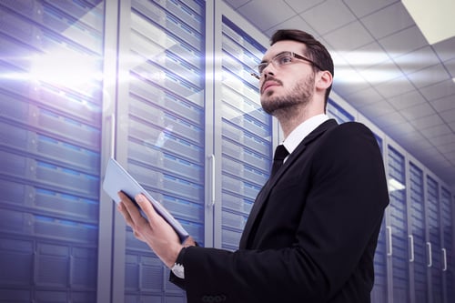 Businessman looking away while using tablet against server room